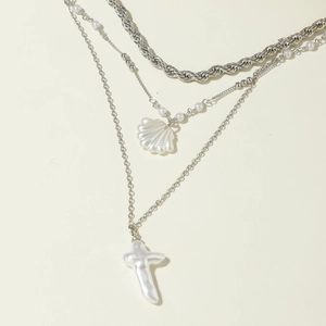 Détail de colliers superposés argentés avec pendentifs coquillage et perle en croix