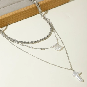 Détail d'un collier multicouche argenté avec pendentifs coquillage et croix sur velours