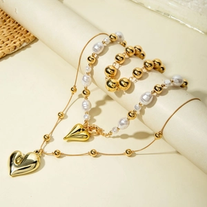 Detalle de collar de capas con colgante de corazón, perlas barrocas y cuentas doradas