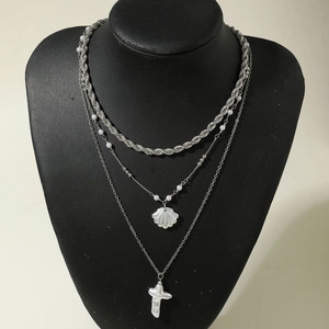 Détail d'un collier multicouche argenté avec perles, breloque coquillage et croix