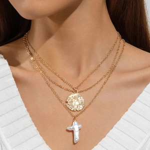 Détail d'un collier multicouche doré avec croix en perle baroque et pendentif pièce