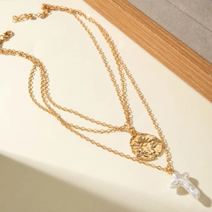 Détail du collier doré double rang avec pendentif martelé et croix en perle baroque