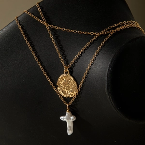 Détail de colliers dorés superposés avec pendentif rond martelé et croix en perle baroque