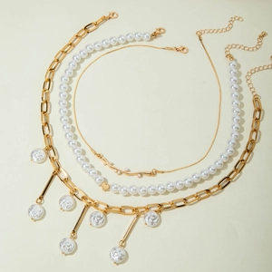 Detalle del conjunto de collares dorados con colgante de corazón, perlas y dije de rama