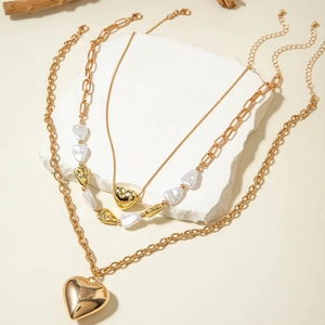 Detalle de collares superpuestos con colgantes de corazón y perlas sobre piedra