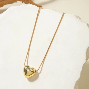 Primer plano de un colgante de corazón dorado pulido con cadena de serpiente fina