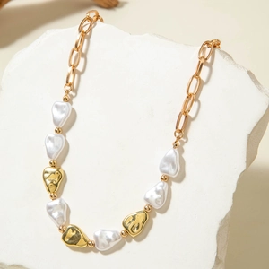 Detalle de perlas barrocas y colgantes de corazón dorados en una cadena de eslabones de oro