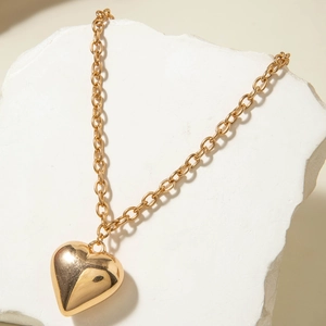 Primer plano de un colgante de corazón 3D en oro pulido con cadena de eslabones y piedra