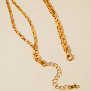 Macro shot of gold tassel necklace featuring flat chain texture and lobster clasp detail