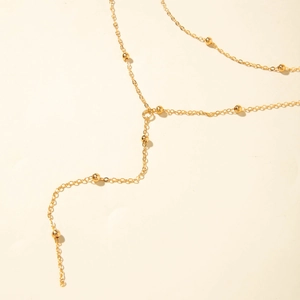 Detail of golden Y-shaped necklace featuring a fine chain with polished beads on white