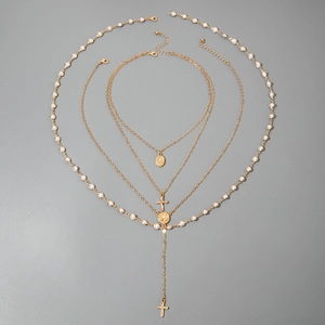 Detailed view of layered gold necklace set with faux pearls, crosses and oval medals