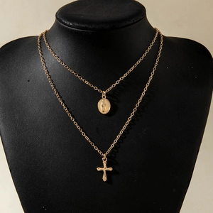 Detail of layered gold-tone necklace featuring oval portrait coin and cross pendants
