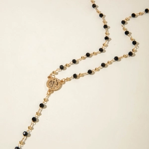 Macro detail of gold-tone religious medal and faceted black beads on Y-shaped necklace