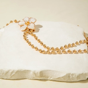 Elegante goldene Perlenkette mit weißem Blumenanhänger auf natürlichem Steinhintergrund