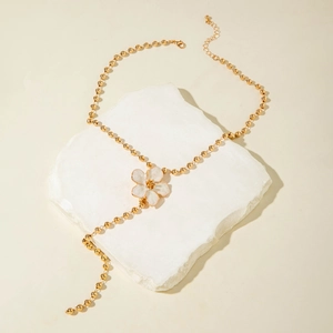 Elegante goldene Perlenkette als Y-Halskette mit weißem Emaille-Blütenanhänger auf Stein