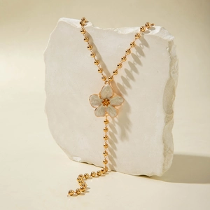 Nahaufnahme einer goldenen Perlenkette mit weißem Blumenanhänger auf einem weißen Stein