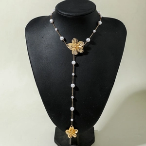 Detail von goldenen Blumenanhängern und weißen Perlen an einer eleganten Y-Halskette