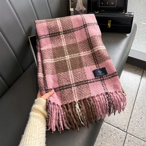 Close-up of pink and brown plaid scarf with fringe and fabric label on leather sofa