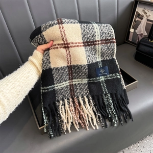 Detailed view of thick plaid scarf with tassels and brand label held by hand