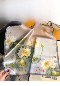 Close-up of square silk scarf featuring lotus and koi fish patterns with satin luster