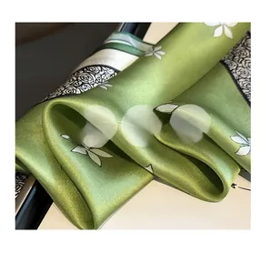 Macro shot showing the satin luster and elegant white floral prints of the green silk scarf