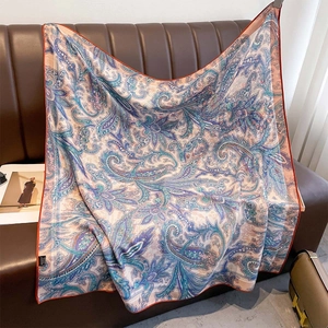 Elegant 100% wool paisley scarf in blue and purple tones draped on a leather sofa