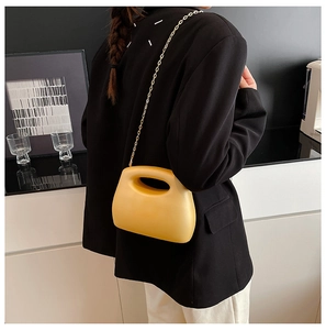 Detail of yellow acrylic evening clutch bag with gold chain strap on a modern background