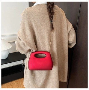 Detail of red acrylic box bag with gold chain strap held by a model in modern setting