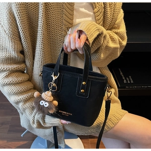 Détail du sac cabas en cuir mat noir avec lettrage doré et accessoire de pompon en peluche