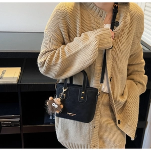 Detail of black matte bucket bag featuring gold hardware and a brown plush doll charm