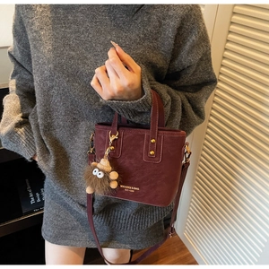 Détail du sac seau bordeaux avec lettrage doré, clous et pendentif peluche à œil
