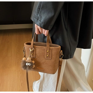 Sac seau marron avec rivets dorés et breloque peluche portée par un mannequin