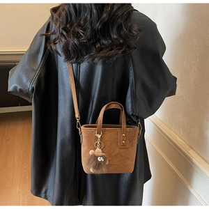 Détail d'un sac seau marron avec breloque en peluche et bandoulière amovible