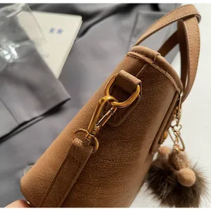 Detail of brown textured leather bag with gold hardware hook and plush ball charm