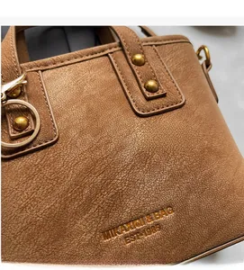 Close-up of brown textured faux leather handbag featuring metal rivets and embossed logo