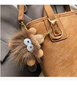 Close-up of creative brown plush monster charm with knit hat on a leather handbag