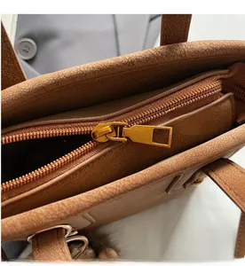 Close-up of smooth gold metal zipper and grainy brown leather texture of a bucket bag