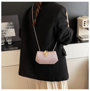 Pink sequin evening clutch bag with golden leaf clasp worn as a crossbody bag over a suit