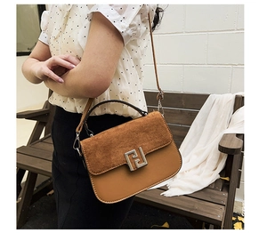 Close-up of brown suede and leather saddle bag with geometric metal lock on a wooden bench