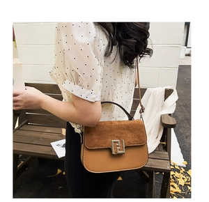 Close-up of brown textured crossbody saddle bag with matte leather and silver buckle