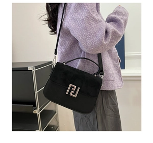 Detail of a black crossbody saddle bag with matte suede texture and silver buckle