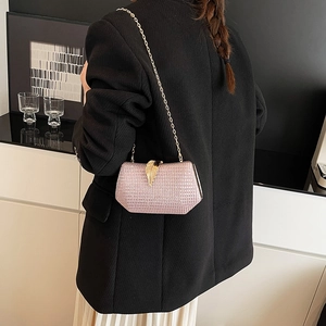 Pink sequin evening clutch bag with golden leaf clasp and chain strap on black blazer