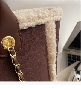 Detailed close-up of brown suede tote bag with cream faux shearling trim and chain strap