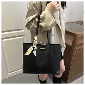 Detail of black leather tote bag featuring a metal bar and decorative silk scarf on handle