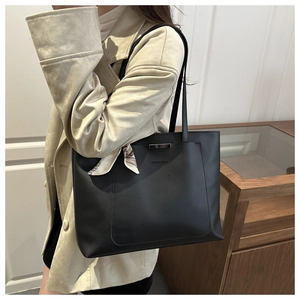 Detail of minimalist black tote bag featuring a decorative silk scarf and metal trim