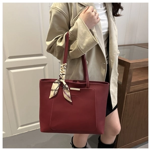 Close-up of burgundy tote bag with metal bar detail and decorative silk scarf accessory
