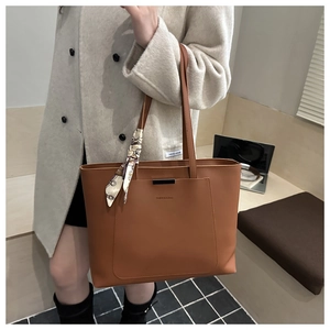 Detail of brown leather tote bag with decorative scarf and metal bar on the front pocket