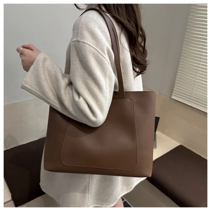 Détail d'un grand sac cabas en cuir mat marron avec poche avant porté à l'épaule par un mannequin