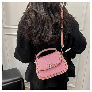 Detail of pink saddle bag with metal clasp worn as a crossbody bag by a model