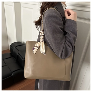 Detail of khaki leather tote bag featuring a decorative silk scarf and front pocket